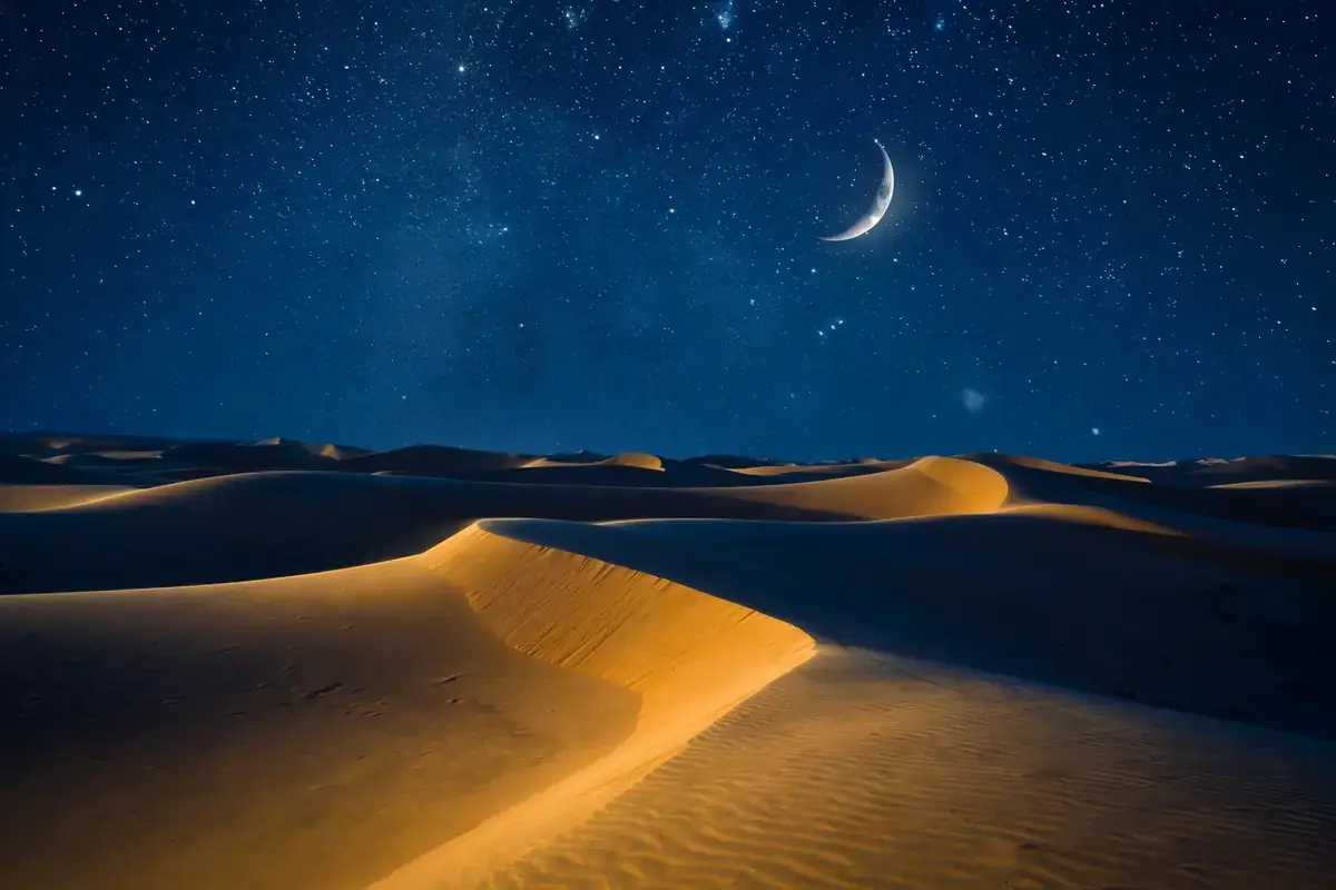 Night sky with stars and crescent moon over desert dunes