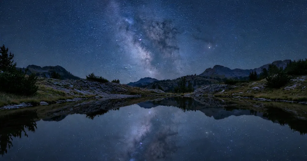 A calm night sky full of stars reflected in still water