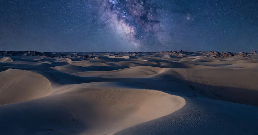 A starry night sky over silent desert dunes