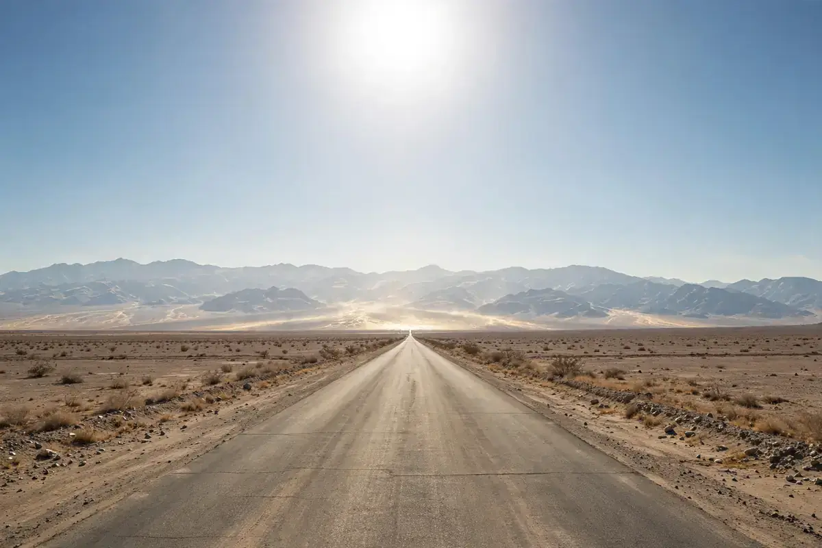 Long desert road stretching to distant mountains under a harsh sun