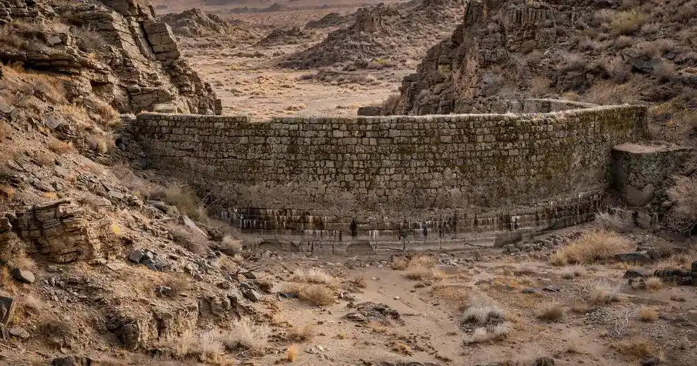 An ancient stone dam wall between two rocky hills